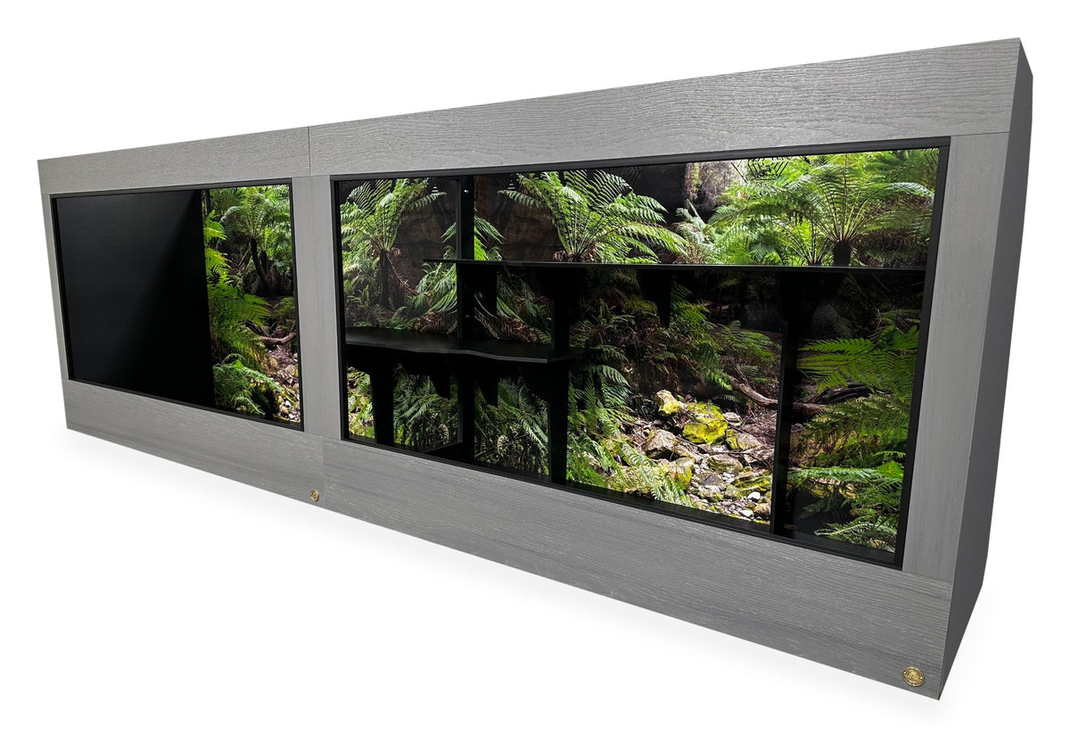 12'x2.5'x4' two-section reptile enclosure with Driftwood gray woodgrain HDPE front frame and black PVC body. Options shown: 10-inch lower frame, Blue Mountains Destinations background and custom shelves.